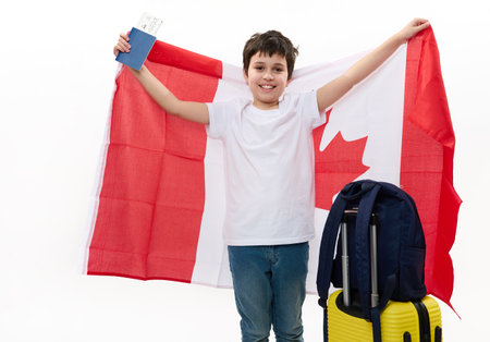 Smart Caucasian teenage boy wearing white t-shirt and blue denim jeans, with backpack, suitcase and boarding pass, carrying Canadian flag, travels to Canada for study exchange experience. Immigrationの写真素材