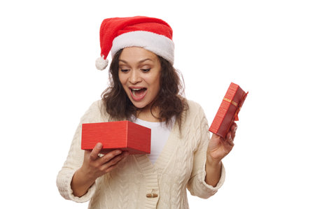 Beautiful African American woman in Santa hat, opens a gift box with a surprise, on white...