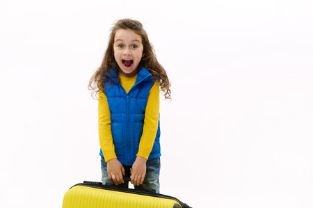 Mischievous little traveler kid girl 5-6 years old, holding yellow suitcase, isolated on white background. Passenger traveling abroad on weekends getaway. Air flight journey concept. Copy ad spaceの写真素材