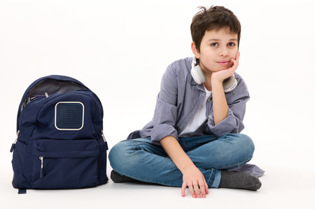 Lovely Caucasian boy teenager, elementary school student wearing casual denim, with blue backpack, confidently looking at camera, isolated on white background. Copy advertising space. Back to schoolの写真素材