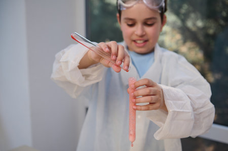 Close-up of the hands of a blurred smart schoolboy, wearing lab coat, holding test tubes with solution coming out, watching the chemical reaction occurs during a chemistry lesson. School. Educationの写真素材