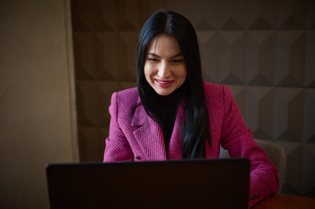 Smiling confident woman entrepreneur 40-45 years old, dressed in a stylish crimson jacket, talking...