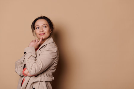 Thoughtful multi-ethnic middle-aged pretty woman putting finger on her chin and dreamily looking aside, reasoning, isolated on a beige background with free advertising space. Women. People. Lifestyleの写真素材