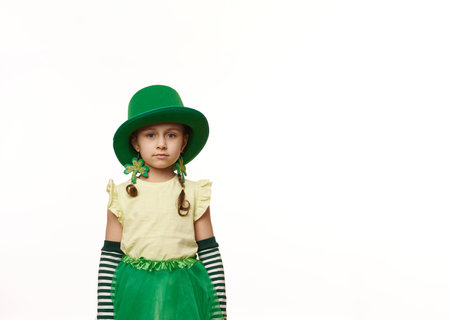 Charming Irish little child girl with two funny pigtails, wearing a Leprechaun carnival costume and clover leaf earrings, looking at camera, isolated over white background. Saint Patricks Day conceptの写真素材