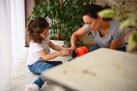 Selective focus on mother and daughter caring for houseplants, watering soil with repotted houseplants, sitting together on floor at home veranda in spring. Environmental conservation. People. Natureの写真素材