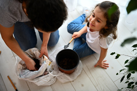 Adorable little child girl sitting on the floor with garden shovel in her hands, smiling to her mom working with fertilized soil during gardening process in the springtime. People and nature conceptの写真素材