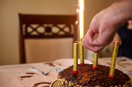 Selective focus on chocolate cake and hand turning on burning candles lighting burning candles on birthday. Celebrations. Life event. Festive mood. Anniversary. Birthday partyの写真素材
