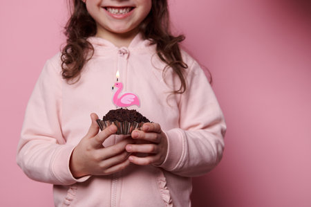 Details: chocolate cupcake with flamingo candle, in the hands of a blurred Caucasian child, lovely...