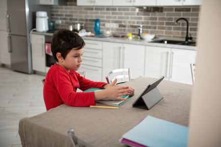 Smart teenage boy, school child doing homework with digital tablet at home. Kid using gadgets to study. Education and distance learning for kids. Homeschooling during quarantine. Online coursesの写真素材