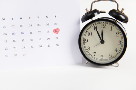 Still life with black alarm clock and a calendar marked with a red marker on the 14th of February. Saint Valentines Day. Festive event. Occasion. Appointment and celebration concept, white backgroundの写真素材