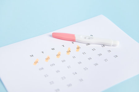 Selective focus. Pregnancy inkjet test and a calendar with dates of the last menstruation marked on blue color background. Womens health. Ovulation date calculation. Planning pregnancy and maternityの写真素材