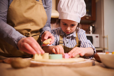 Selective focus on an inspired little child girl in chefs hat preparing gingerbread biscuits, cutting dough using cookie cutters, under the guidance of her mom in the home kitchen. Easter conceptの写真素材