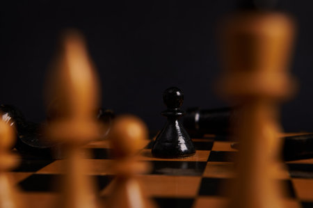 Selective focus on black wooden chess piece, a pawn moving and white pieces on blurred foreground, isolated on black background. Symbolic illustration of total war, disagreement, disaster and failureの写真素材
