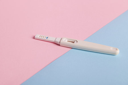 Still life. Pregnancy test with positive result between HCG hormone in female urine, isolated on pink and blue pastel background. Rapid diagnosis of pregnancy. Womens health and fertility conceptの写真素材