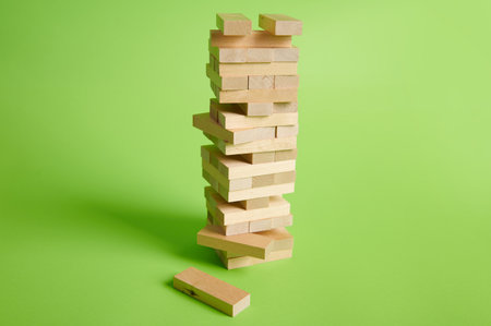 Wooden block tower on green background. Destruction of blocks. Entertainment activities. Board game game of physical and mental skill, developing fine motor skills. Construction and building conceptの写真素材