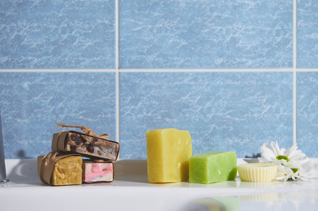 Still life with organic cold pressed soap bars with herbal ingredients and essential oils, for purity, home spa, skin and body care, on the bathroom wash basin against blue marble wall backgroundの写真素材