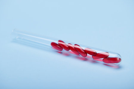 Still life with soft translucent gelatin capsules of red color with essential oils, omega-3 or fat-soluble vitamins inside a test tube, isolated blue background, copy space. World Health Day conceptの写真素材