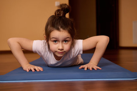 Close-up front view of Caucasian determined active little girl in white t-shirt and sportswear,...