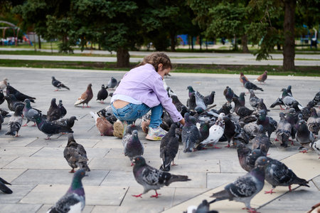Little child girl 5 years old, feeding rock pigeons in the park square. The concept of installing of love, care and compassion for wild animals leaving in the street from childhood. People and natureの写真素材
