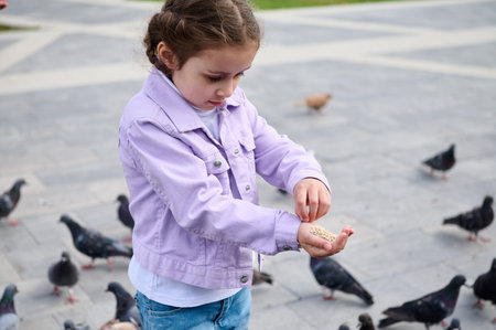 Caucasian adorable little child girl feeding rock doves in the city square. The concept of childhood, care and love for animalsの写真素材
