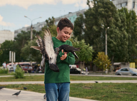 Happy positive smiling multi-ethnic teenage boy feeding pigeons on the square on a sunny spring day. The concept of love, care and compassion for wild animals. People. Nature. Lifestyleの写真素材