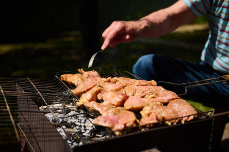 Close-up. Selective focus. Man grilling food, meat on over coals on barbeque grill. BBQ. Barbecue outdoors. Food. Nourishmentの写真素材