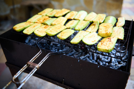Close-up view of zucchini slices, being seasoned, marinated and cooked over flaming charcoal barbecue grill in a backyard. BBQ party. The concept of preparing food in the open air and summer chill outの写真素材