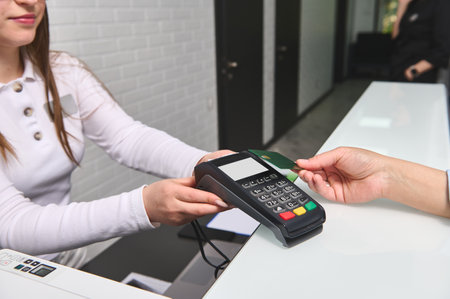 Close-up view of customers hand paying by credit card and entering pin code on reader holded by a...