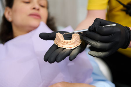 Closeup gloved hands of orthodontist holding dental plaster mold over blurred background of a woman...