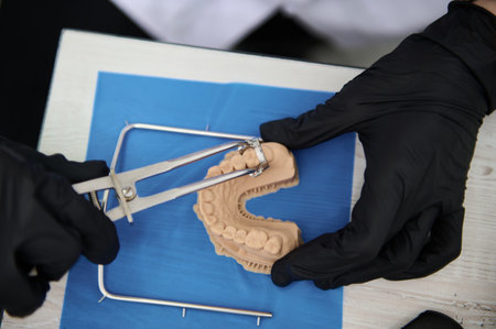 Directly above doctor othodontist working with plaster cast of human jaw. Close-up hands in black...