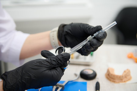 Close-up hands of dentist doctor in black medical sterile gloves, holding syringe for local dental anesthesia. Dentistry. Dental practice. Orthodontics. Maxillofacial surgery. Healthcare and medicineの写真素材
