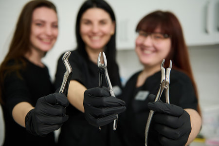Stainless steel dental pliers, extraction forceps for removing extracting teeth in the hands of blurred smiling female dentists doctors, maxillofacial surgeons, orthodontists in black medical uniformの写真素材