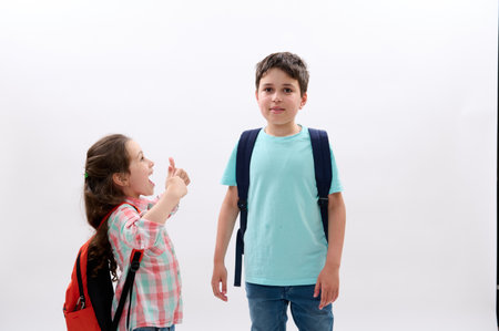 Smart diverse school kids with backpacks, little girl smiles looking at her older brother, going to the school, enjoying first school day on new semester of academic year, isolated white backgroundの写真素材