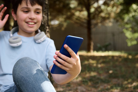 Selective focus on modern smartphone in the hand of a preteen boy talking via video link while...
