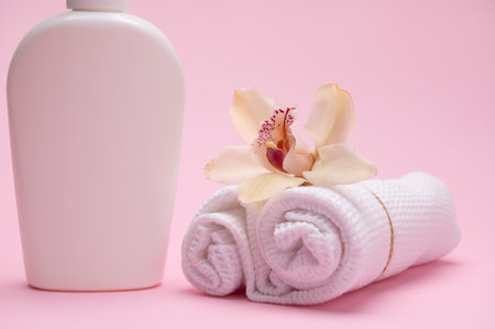 Selective focus on yellow orchid flower on rolled tied white waffle towels, near a bottle with intimate hygiene shower gel, isolated on pink color background. Mockup. Template. Copy advertising spaceの写真素材