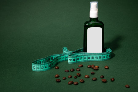 Still life. Cosmetic bottle from dark glass with a massage oil, measure tape and coffee beans scattered on green background. Anti-cellulite, weight loss, blood circulation improvement and spa concept.の写真素材