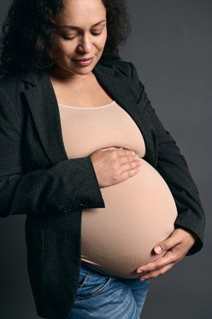Close-up multi-ethnic beautiful woman expecting a baby, touching her pregnant belly, smiling,...