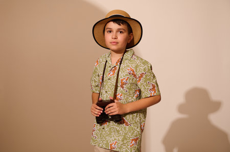 Handsome Latin American teenage boy in stylish casual summer clothes and straw hat, a happy traveler tourist adventurer, holding binoculars, looking confidently at camera, isolated studio background.の写真素材