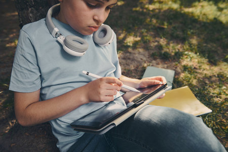 Handsome smart school boy using a digital tablet and stylus pen, drawing, sketching, enjoying his creative hobby outdoors. People. Leisure activity. Learning. Lifestyle. Creativity.の写真素材