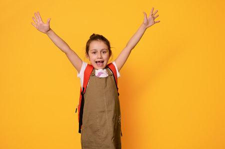Authentic portrait of Caucasian elementary age girl, school child dressed in casual wear, expressing positive emotions, isolated on orange studio background. Back to school. Kids and education conceptの写真素材