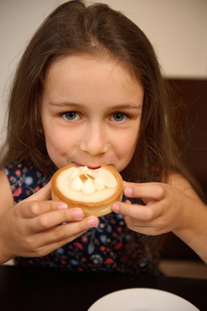 Close-up portrait of a Caucasian cute little child girl tasting a sweet French baked dessert - a lemon tartlet, smiles looking at cameraの写真素材