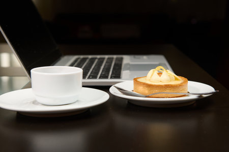 Still life with food and electronical device. A sweet delicious tartlet, cup of coffee over laptop background. Copy advertising spaceの写真素材