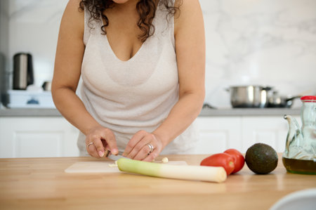 Details on female chef's hands chopping leek and garlic on cutting board in the minimalist home...