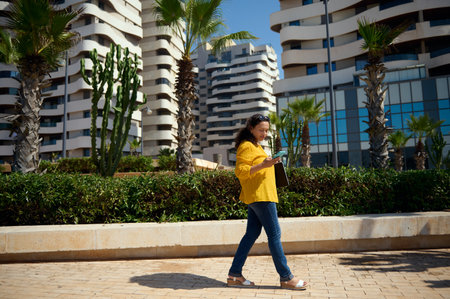 Side portrait of a multi-ethnic curly haired authentic woman, strolling the street, checking her...