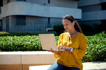 Confident Latin American middle aged woman, successful entrepreneur, businesswoman in casual clothes, sales manager online working on laptop outdoor. People. Internet. Business. Recruitment and careerの写真素材