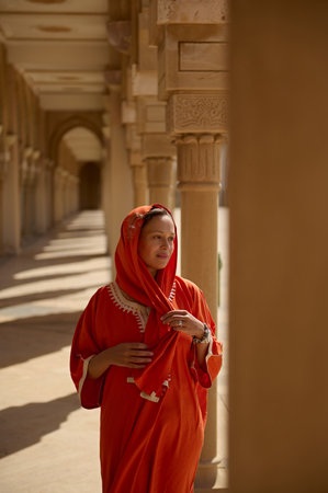 Beautiful Middle Eastern Muslim woman with head covered in hijab, walks along the marble columns in the mosque territory, dreamily looking aside, visits the sacred place. People and religion conceptの写真素材