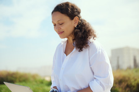Closeup portrait of a confident charming ethnic curly haired female freelancer entrepreneur, programmer developer telecommuting outdoors. People. Online job. Remote work and internet business conceptの写真素材