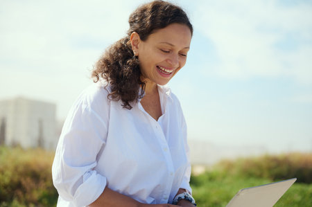 Beautiful multi ethnic young female manager smiling broadly while online working outdoors, using laptop. Confident closeup portrait of a businesswoman expressing positive emotions, enjoying remote jobの写真素材