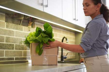 Beautiful housewife standing by kitchen counter and sorting fresh organic spinach and salad leaves,...