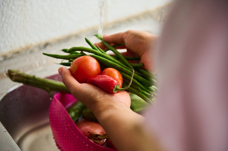 Closeup hands of a housewife woman holding fresh organic vegetables and washing under running water in the sink at home kitchen, cooking yummy vegetarian meal. Food. Healthy eating . Dieting conceptの写真素材